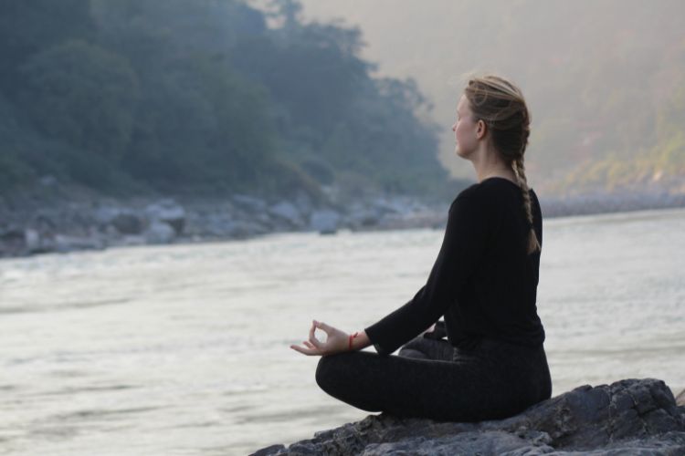 Female doing Meditation by the Ganga River in Rishikesh