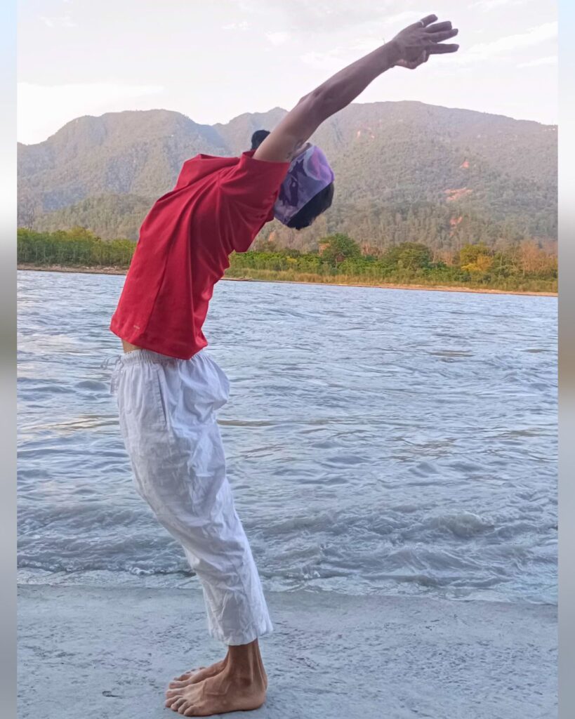 A person standing with arms lifted straight overhead and a slight backbend in Hastauttanasana