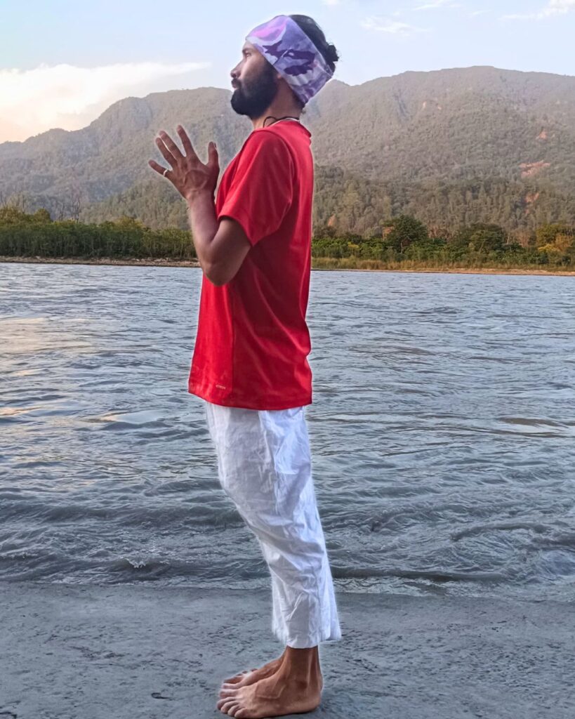 A person stands upright with feet together and palms pressed together at the chest, in Pranamasana.