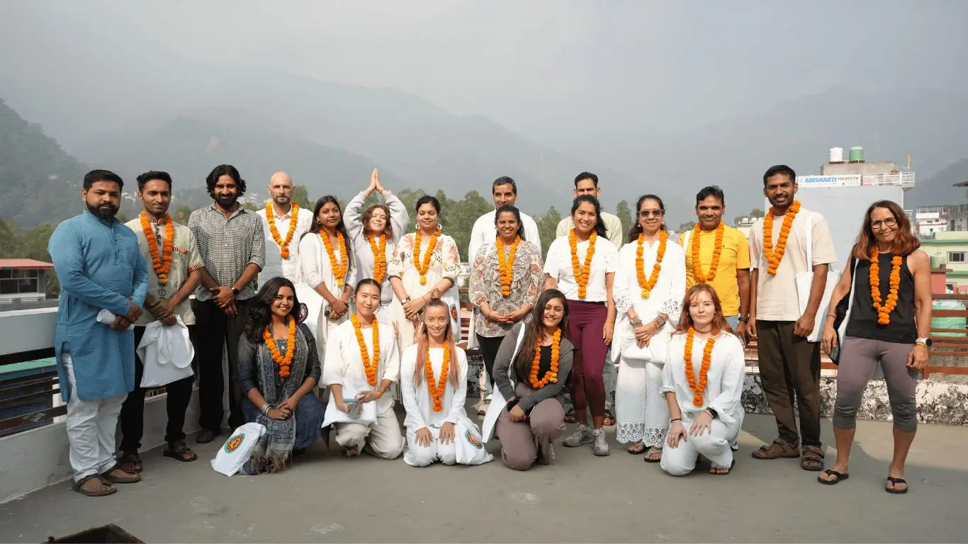 Group photo of 200 hour yoga teacher training students and teachers at yoga ashram in Rishikesh with Himalayan mountain backdrop