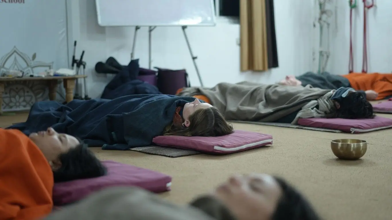 Participants lying in relaxation pose during a sound bath meditation with Tibetan singing bowls at a sound healing training in Rishikesh, India.