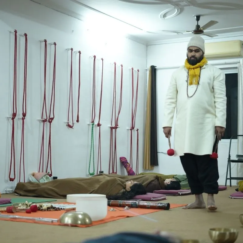 Sound healing instructor performing a singing bowl therapy session while students relax during a sound bath training in Rishikesh, India.