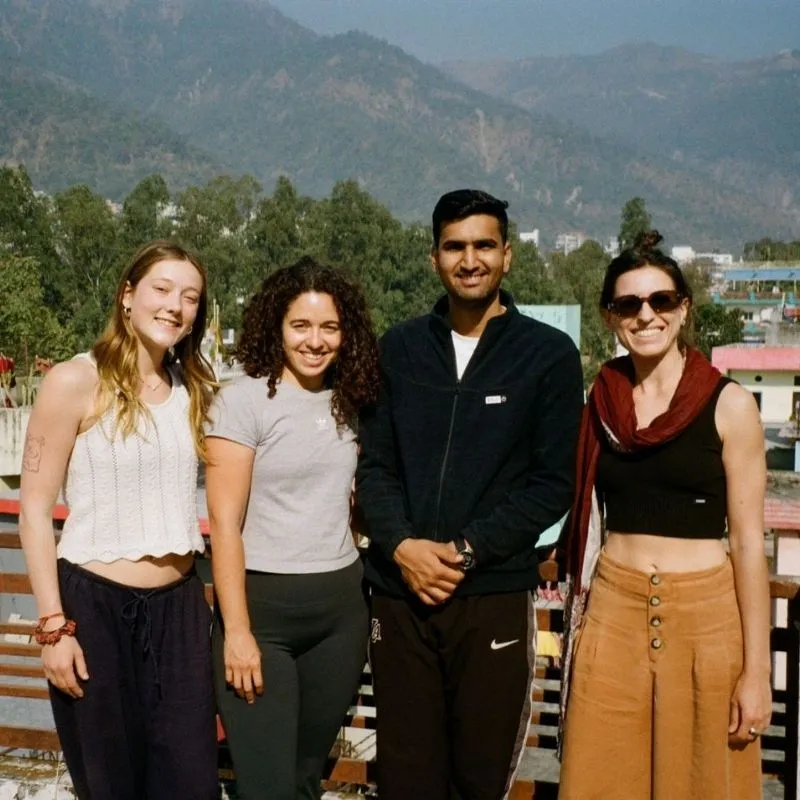 A diverse group of smiling students participating in a sound healing training course on a rooftop with a scenic mountain backdrop.