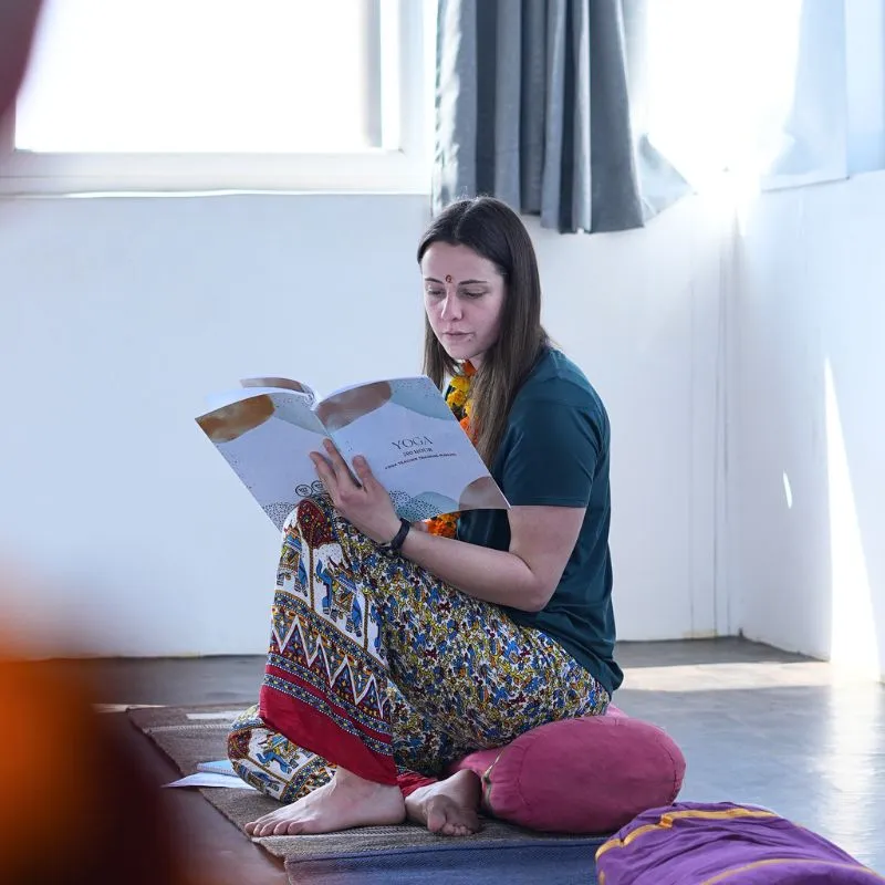 Student studying yoga philosophy during 100 hour yoga teacher training in Rishikesh India while sitting on a yoga mat in a peaceful classroom.
