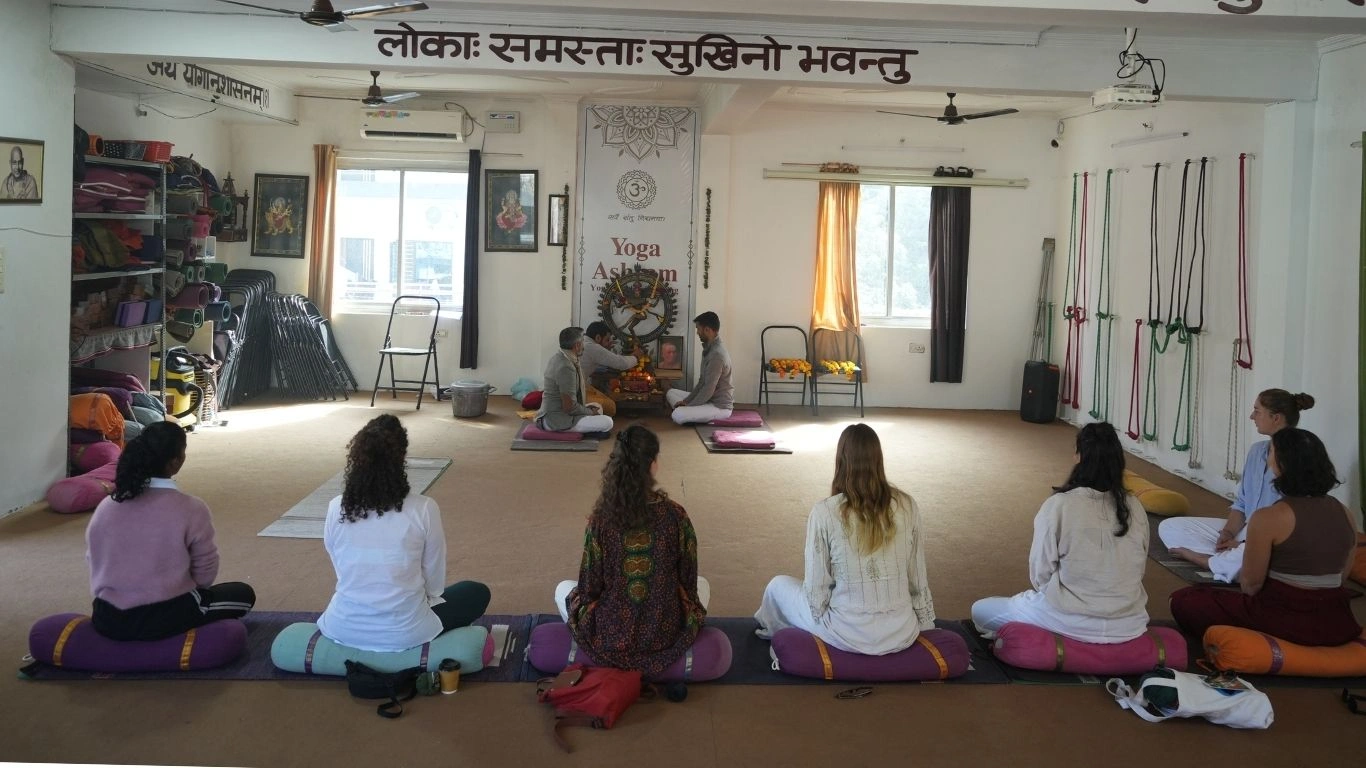 Students attending a traditional yoga class during 200 vs 300 Hour Yoga Teacher Training in Rishikesh, India, learning meditation and yogic rituals inside a yoga ashram.