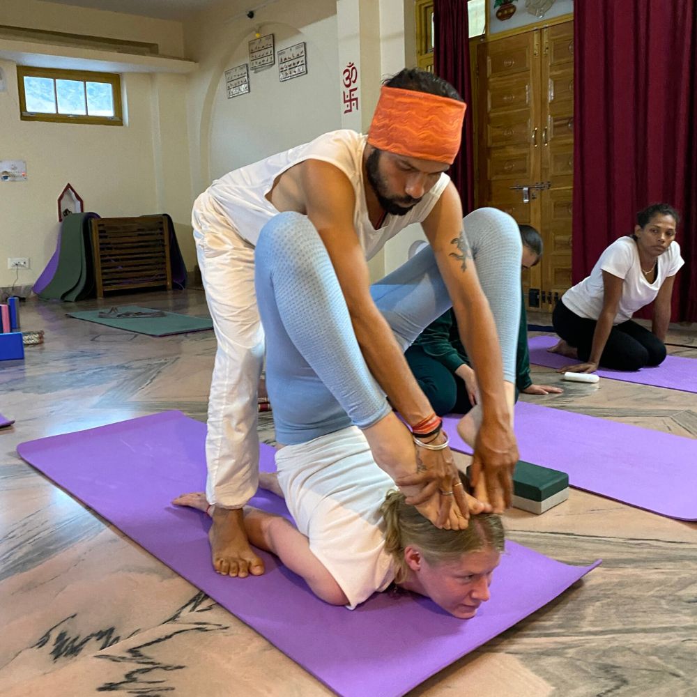 300 hour yoga teacher training in rishikesh, yoga teacher helping student to hold asana