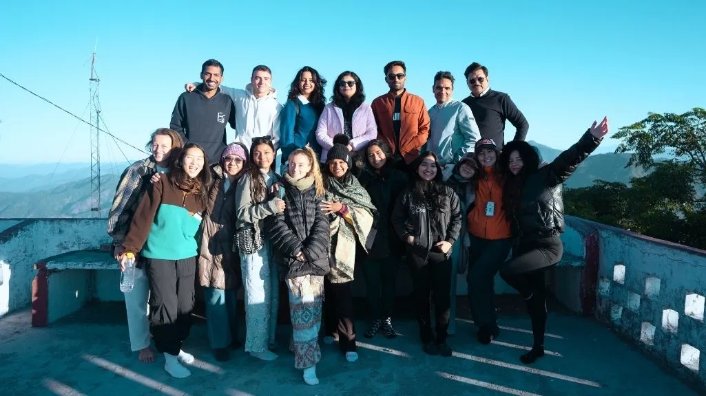 A happy group of international students posing together on a mountain rooftop during a 7 days yoga retreat in Rishikesh, India.