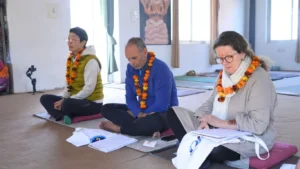 Mature students sitting on meditation cushions with study materials, showing how a 40 plus year old can do yoga teacher training through dedicated theory and practice sessions in a traditional shala.