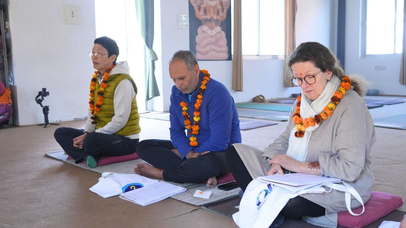 Mature students sitting on meditation cushions with study materials, showing how a 40 plus year old can do yoga teacher training through dedicated theory and practice sessions in a traditional shala.