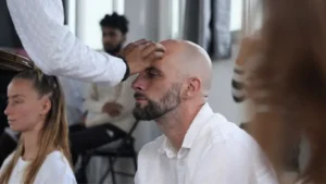 A close-up shot of a practitioner receiving a blessing or Tilak on the forehead during a ceremony at Rishikesh Yoga Valley. This ritual is a significant aspect of a traditional yogic lifestyle, emphasizing the opening of the third eye and spiritual focus. The practitioner is dressed in white, surrounded by others in a serene, meditative environment.