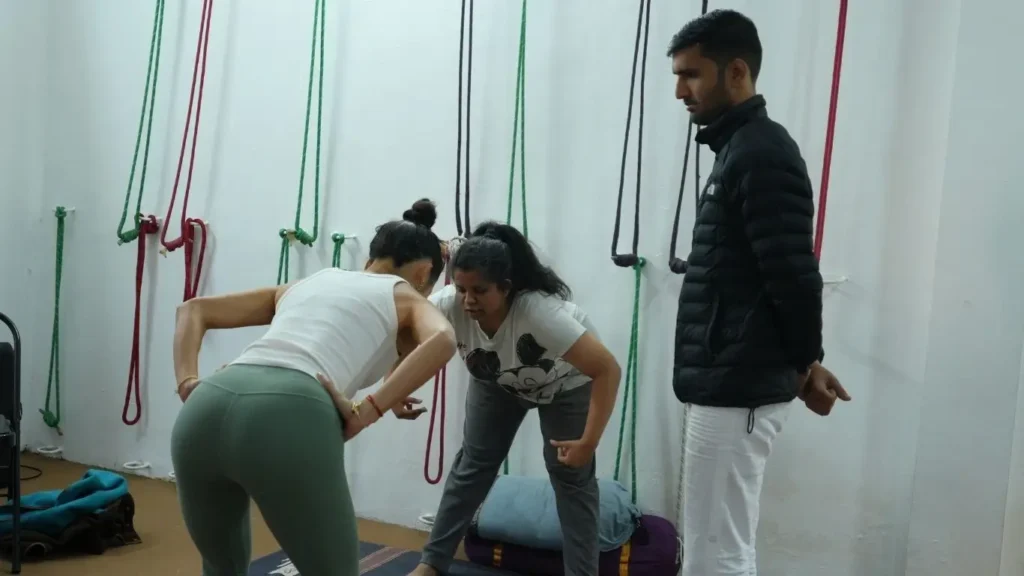 Yoga instructor correcting a student’s posture during practical training, helping future teachers gain skills to build a yoga business after certification.