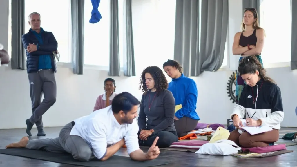 A lead yoga instructor demonstrates a posture to international students during a training session at Rishikesh Yoga Valley. This professional certification is a key step for those researching the yoga teacher salary worldwide and seeking to build a sustainable career in the wellness industry.