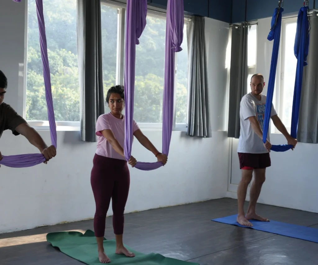 Students practicing aerial yoga using hammocks during yoga teacher training in Rishikesh, India.