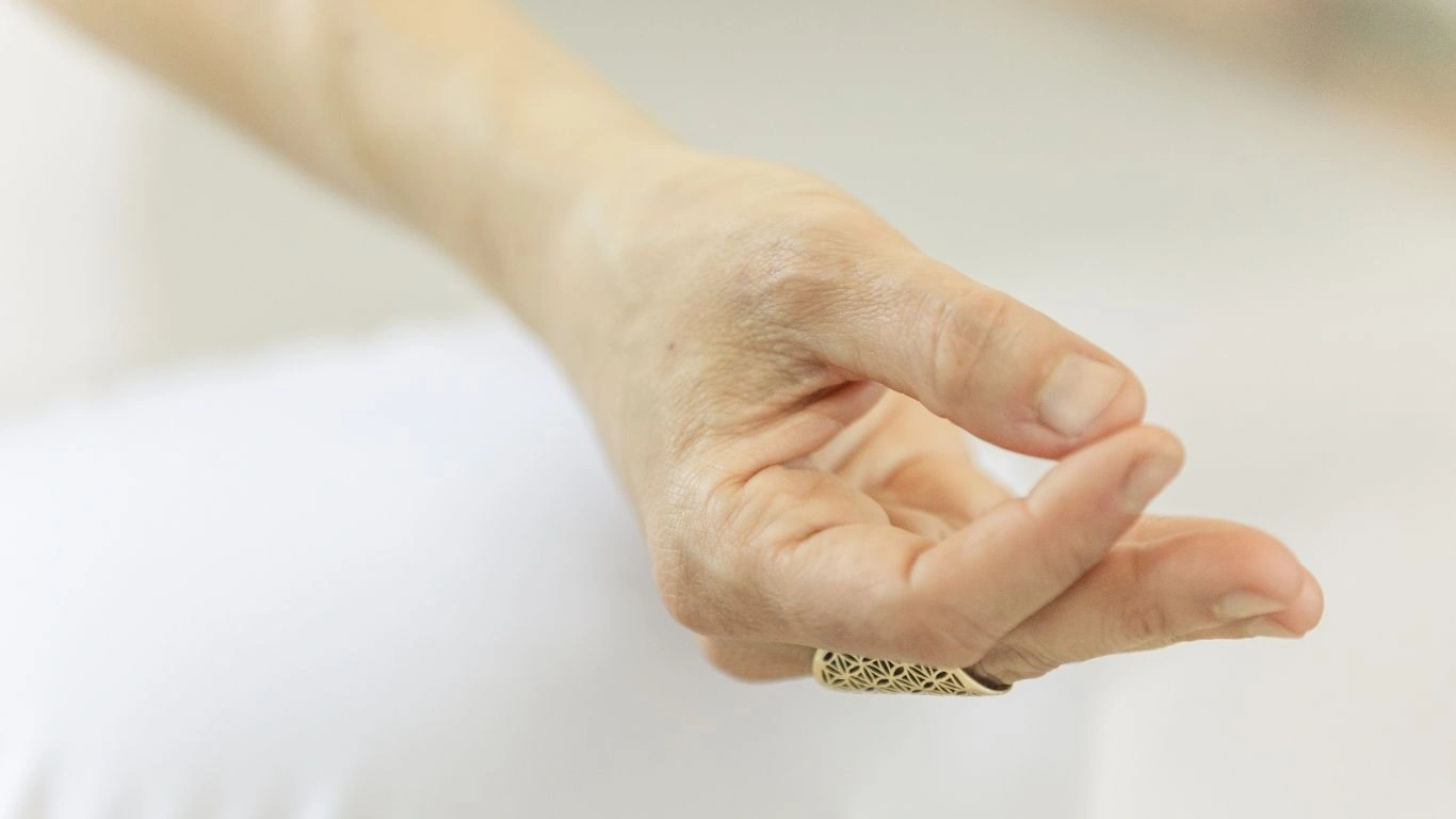 Close-up of a student practicing Gyan Mudra during a 200 hour Kundalini yoga teacher training in Rishikesh, India, featuring a hand in a meditative gesture with a sacred geometry ring.
