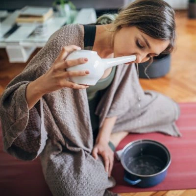 Woman using neti pot for Jala Neti nasal cleansing at home to improve sinus health and breathing