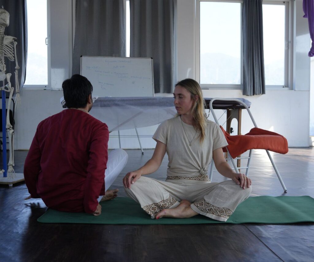 Yoga teacher guiding a student in posture alignment during yoga teacher training class in Rishikesh, India.