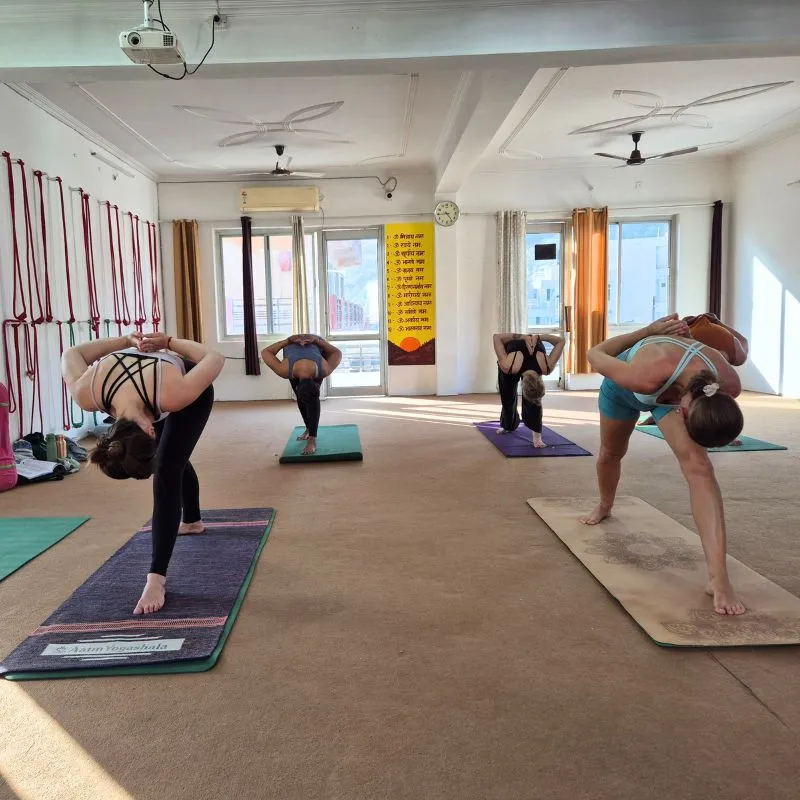 Students practicing standing twisting yoga pose during 100 hour yoga teacher training in Rishikesh India inside a traditional yoga studio