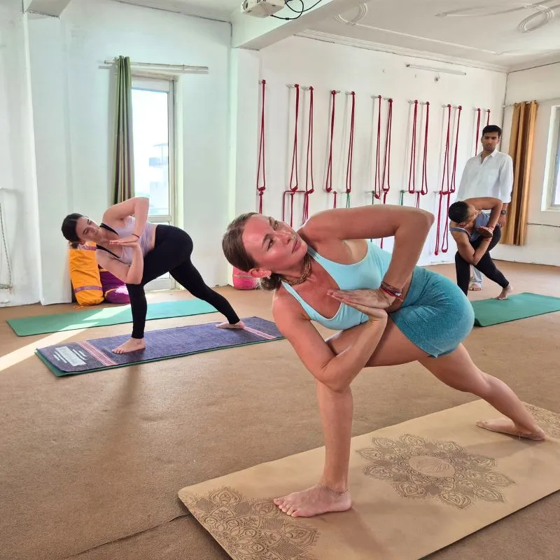Students practicing twisting yoga pose during 100 hour yoga teacher training in Rishikesh India inside yoga studio