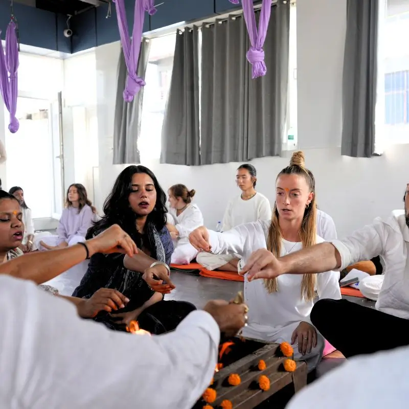 Students participating in traditional fire ceremony during 14 days yoga retreat in Rishikesh India inside a meditation hall