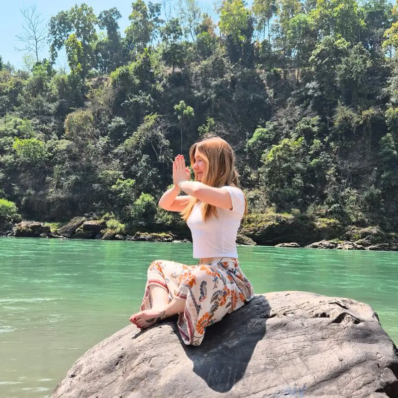 Student practicing meditation near the Ganga River during 14 days yoga retreat in Rishikesh India surrounded by natural Himalayan scenery