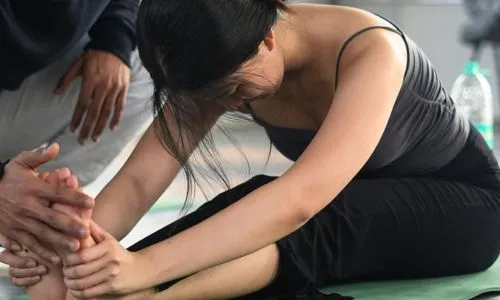 Student practicing seated forward stretch during 50 hour yoga teacher training in Rishikesh India with guided yoga adjustment