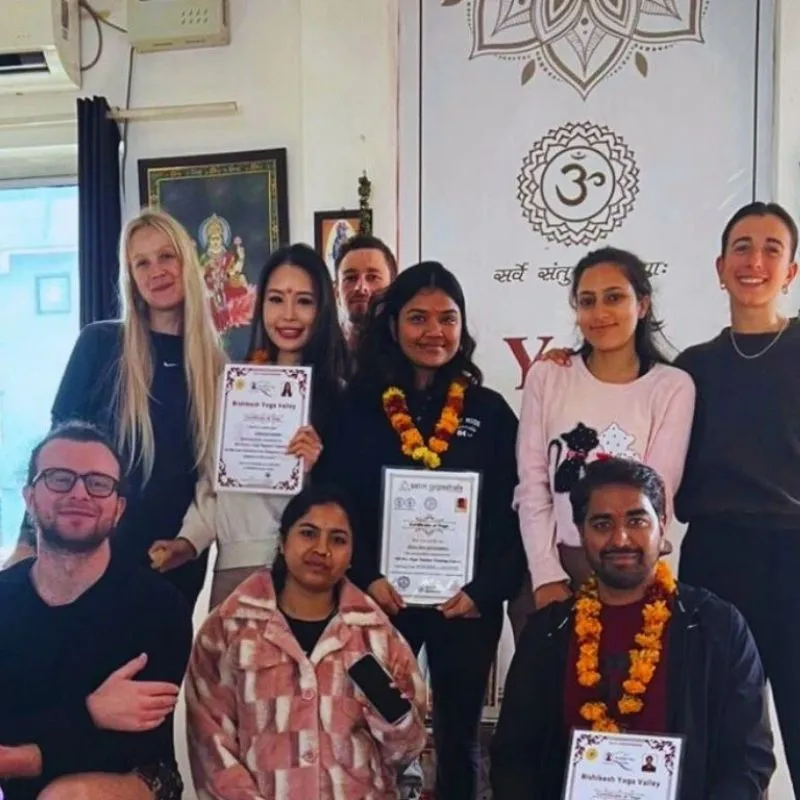 Students holding certificates after completing 50 hour yoga teacher training in Rishikesh India inside a traditional yoga school