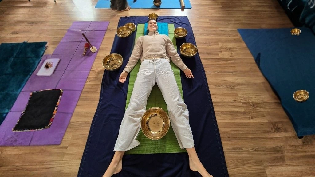 Person lying in a sound bath healing therapy session surrounded by Tibetan singing bowls for deep relaxation, meditation, stress relief, and holistic wellness