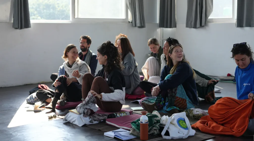 Diverse group of yoga students sitting together on the floor, laughing and bonding during a 200 hour yoga teacher training lecture