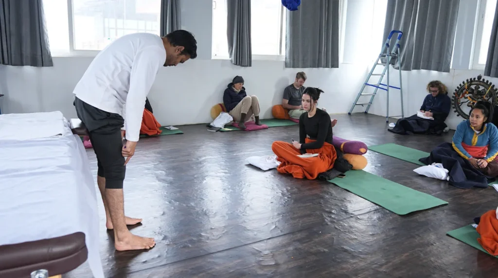 Yoga instructor demonstrating proper body alignment to attentive students taking notes in a 200 hour yoga teacher training classroom setting