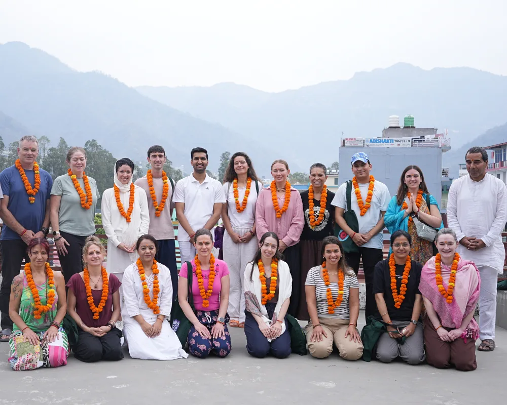 International yoga students wearing marigold garlands celebrating their 300 hour yoga teacher training in Rishikesh with Himalayan mountains in the background