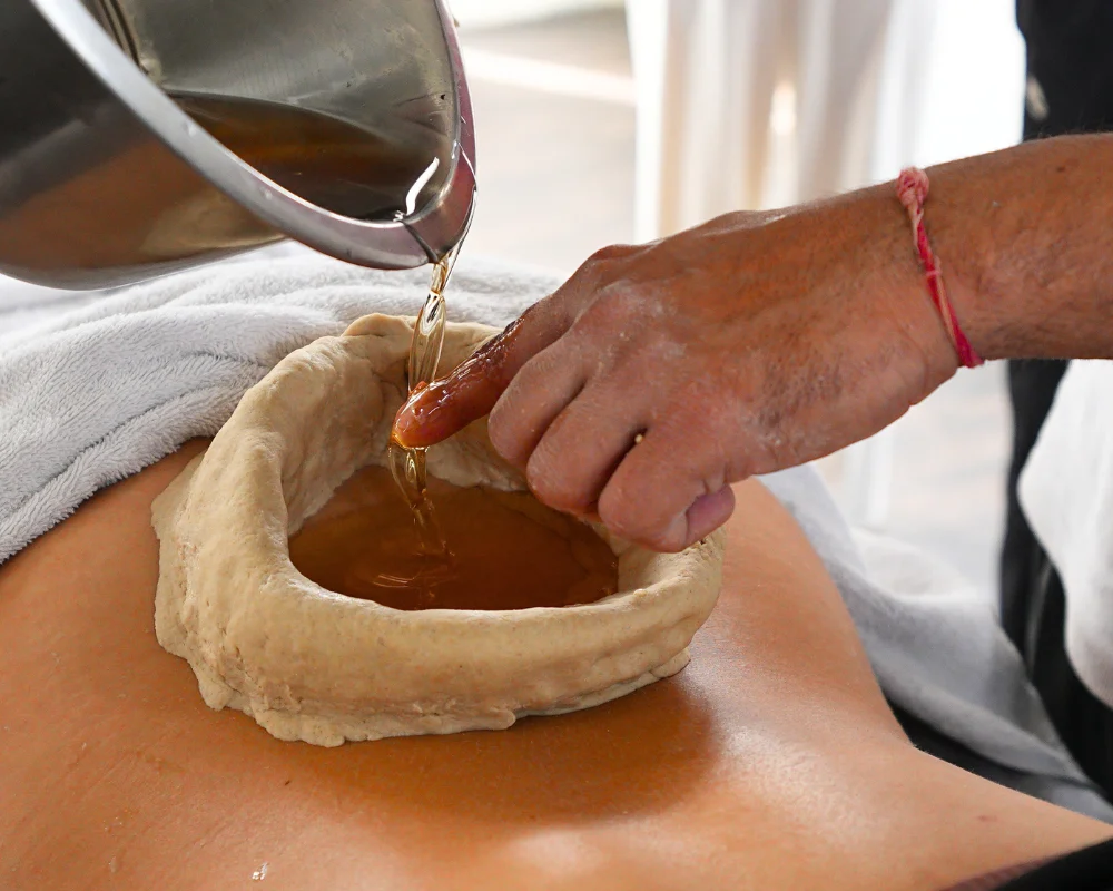 Ayurvedic Kati Basti treatment being performed on lower back during a 300 hour yoga teacher training in Rishikesh
