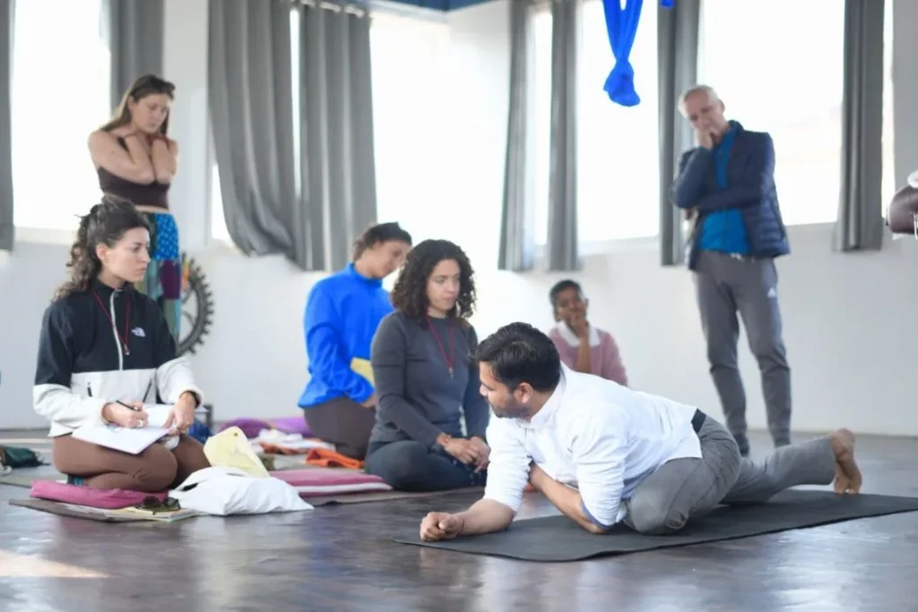 A lead yoga instructor demonstrating body alignment adjustments on a mat to a group of attentive teacher training students.