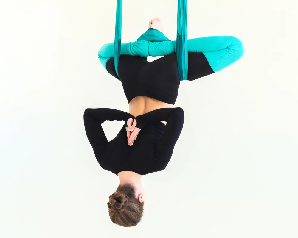 Yogini practicing an inverted butterfly posture with hands in reverse prayer during Aerial Yoga Teacher Training in Rishikesh, India