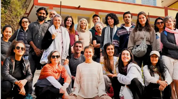 A large diverse group of international yoga students and local instructors smiling together outside an ashram building during a cultural immersion during yoga ttc in rishikesh.