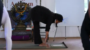 Student practicing a standing forward fold during a 200 hour yoga teacher training class in Rishikesh, explaining how difficult is 200 hour yoga teacher training for beginners.