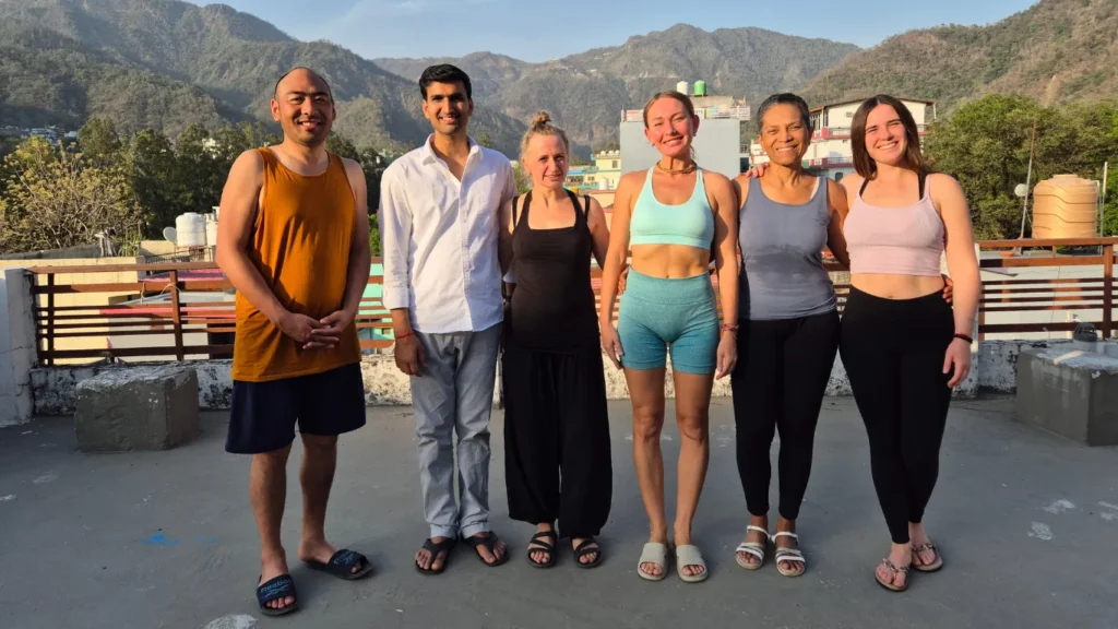 A diverse group of smiling yoga students standing on a rooftop, proving that answering how difficult is 200 hour yoga teacher training is worth the effort.