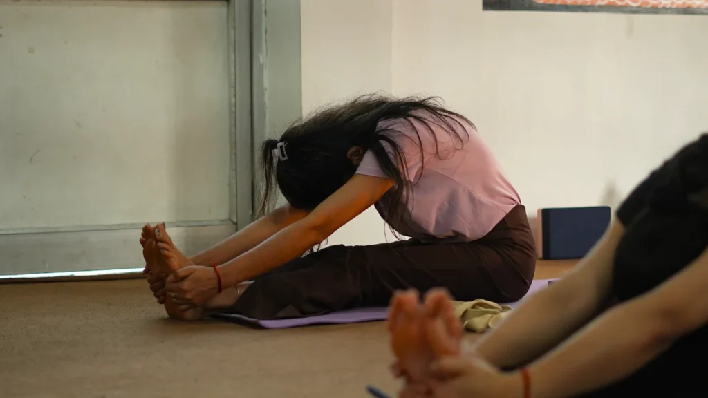 A student performing a seated forward bend pose on a mat, demonstrating how difficult is 200 hour yoga teacher training physically.