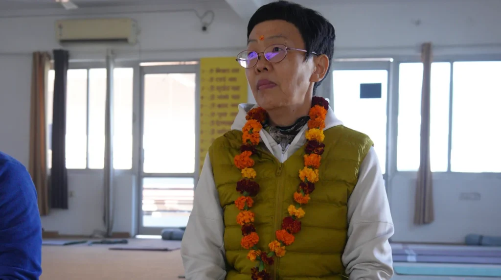 A focused yoga student wearing a traditional marigold flower garland (mala) and a tilak mark on their forehead during an opening ceremony for a 200-hour yoga teacher training.