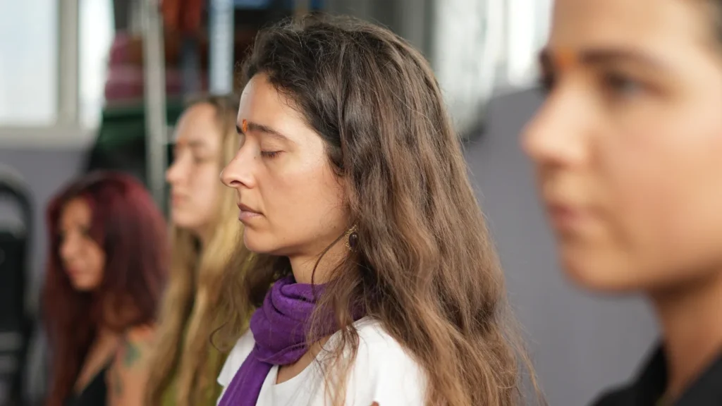 Close-up profile of a female student with a tilak meditating with her eyes closed alongside peers, showing how difficult is 200 hour yoga teacher training emotionally and spiritually