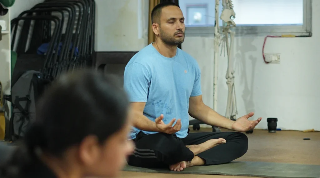 A male student meditating in cross-legged pose during a yoga anatomy class, illustrating why the school you choose matters more than you think.