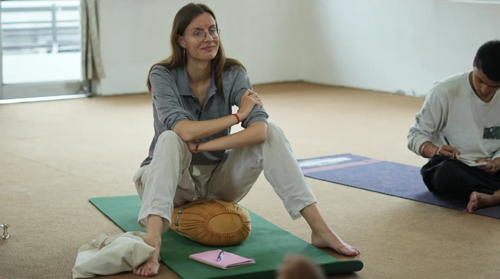A smiling yoga student seated on a bolster during a theory lecture, demonstrating why the school you choose matters more than you think.