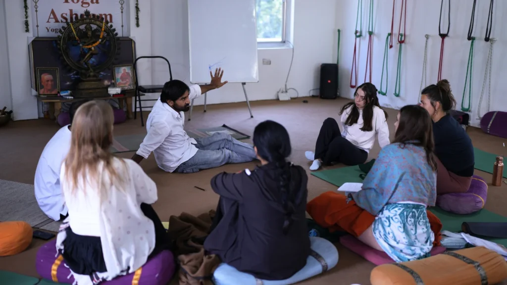 An Indian yoga teacher leading a theory lecture for international students sitting in a circle, highlighting how difficult is 200 hour yoga teacher training academically.