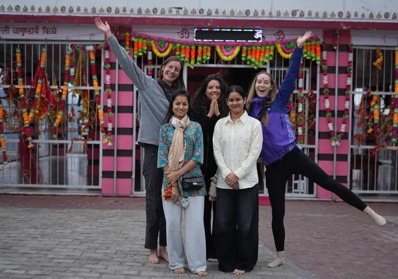 A happy group of yoga students posing outside the decorated Kunjapuri Devi Temple entrance during a yoga teacher training in rishikesh kunjapuri outing.