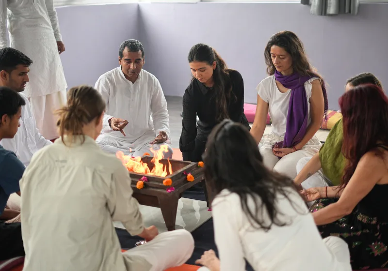 Students and a guru gathering around a sacred Havan fire pit during a traditional yoga teacher training in rishikesh opening ceremony.