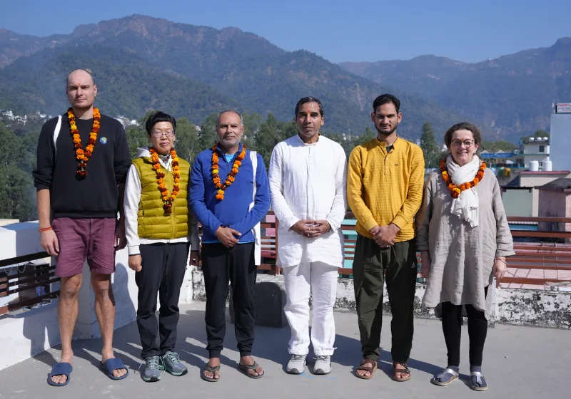 Students and gurus gathered on a rooftop with mountains in the background during a yoga teacher training in rishikesh opening ceremony, wearing traditional marigold garlands.
