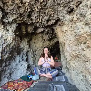A yoga student meditating cross-legged with hands in prayer pose inside a natural rock cave during the 100 hour Kundalini yoga teacher training in Rishikesh.
