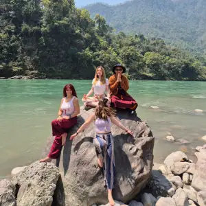 A group of yoga practitioners meditating and sitting together on a large rock along the Ganges River during the 100 hour Kundalini yoga teacher training in Rishikesh.