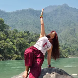 Woman performing a side plank yoga pose on a rock beside the Ganges River during the 100 hour Kundalini yoga teacher training in Rishikesh.
