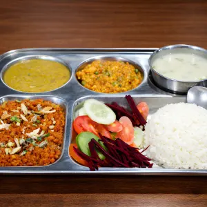 A traditional stainless steel compartmentalized thali tray with rice, lentils, vegetables, fresh salad, and dessert served during the 200 hour Kundalini yoga teacher training in Rishikesh.