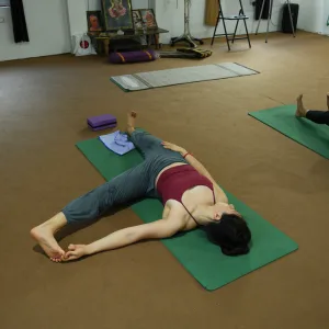 Student practicing a wide-legged supine toe-hold stretch on a green mat inside the studio during the 100 hour Kundalini yoga teacher training in Rishikesh.